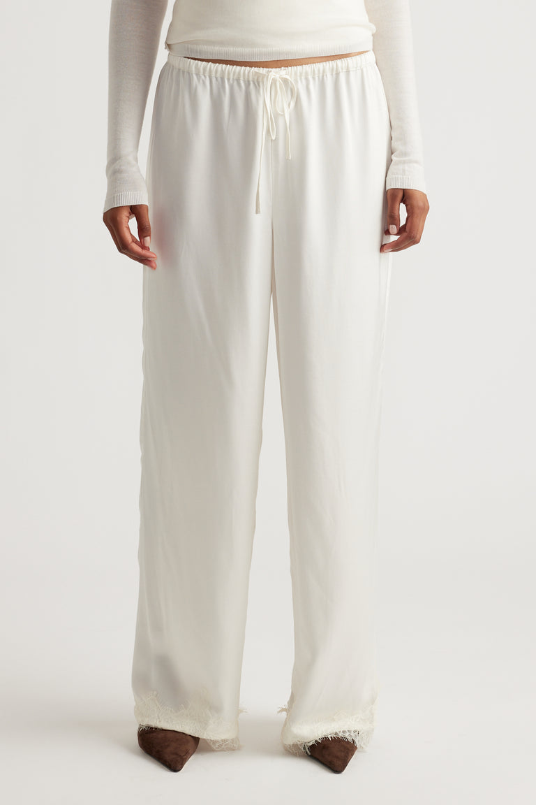 Front view of a woman wearing loose, ivory satin pants with delicate lace trim at the hem, styled with a fitted long-sleeve top