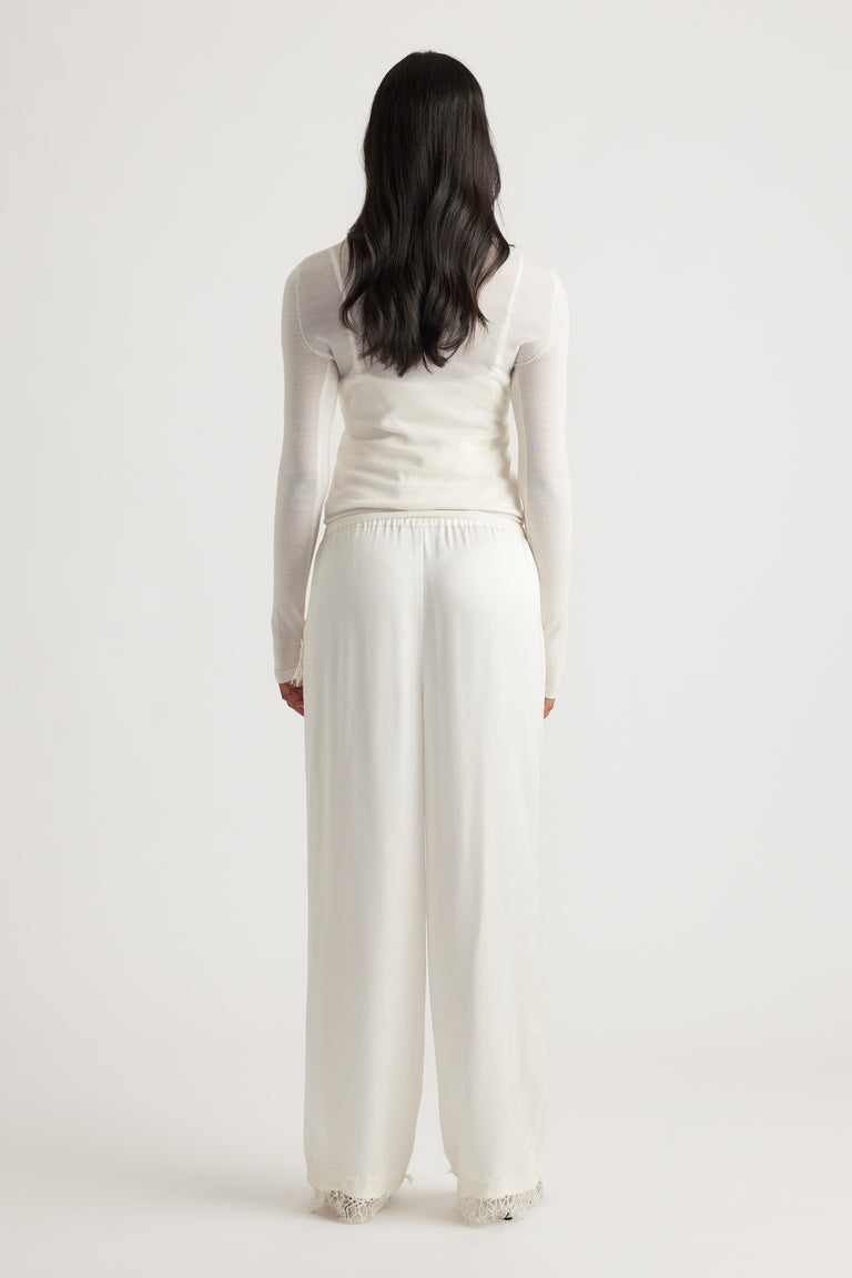 Woman wearing flowing ivory satin pants with delicate lace trim at the hem, paired with a fitted sheer long sleeve top.