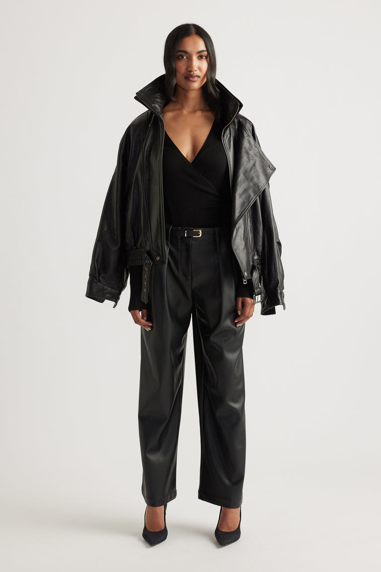 Woman wearing wide-leg black faux leather pants with pleats and a belted waist paired with a black wrap top and jacket