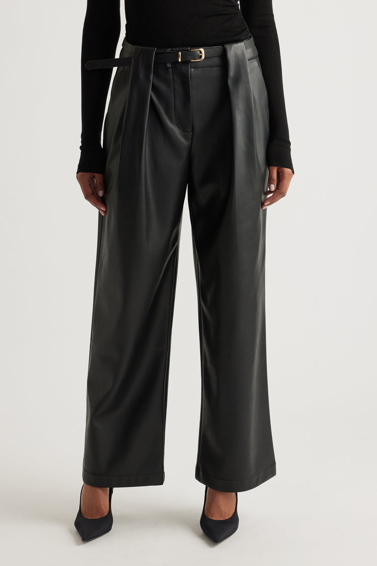 Front view of wide-leg black faux leather pants styled with a slim belt and paired with pointed black heels