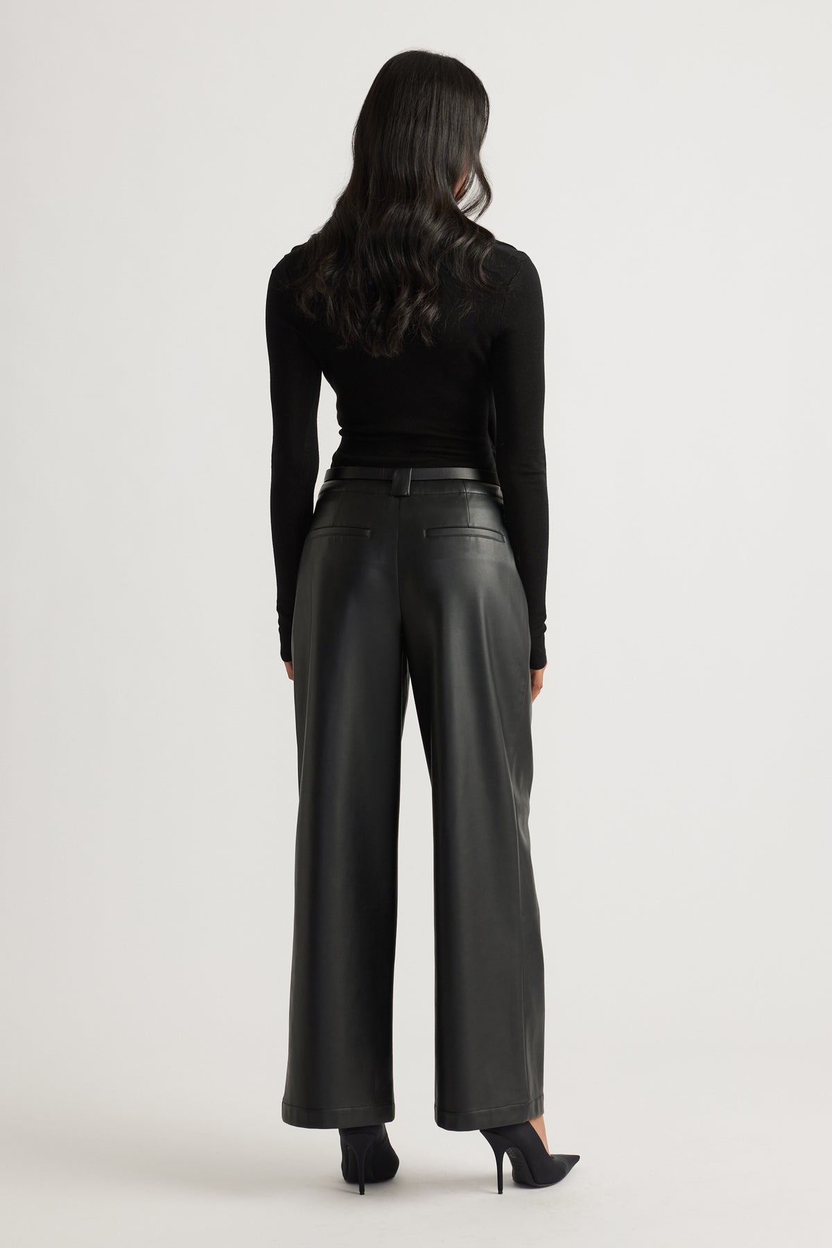 Back view of black wide-leg faux leather pants paired with a fitted long sleeve top and heels for a sleek look