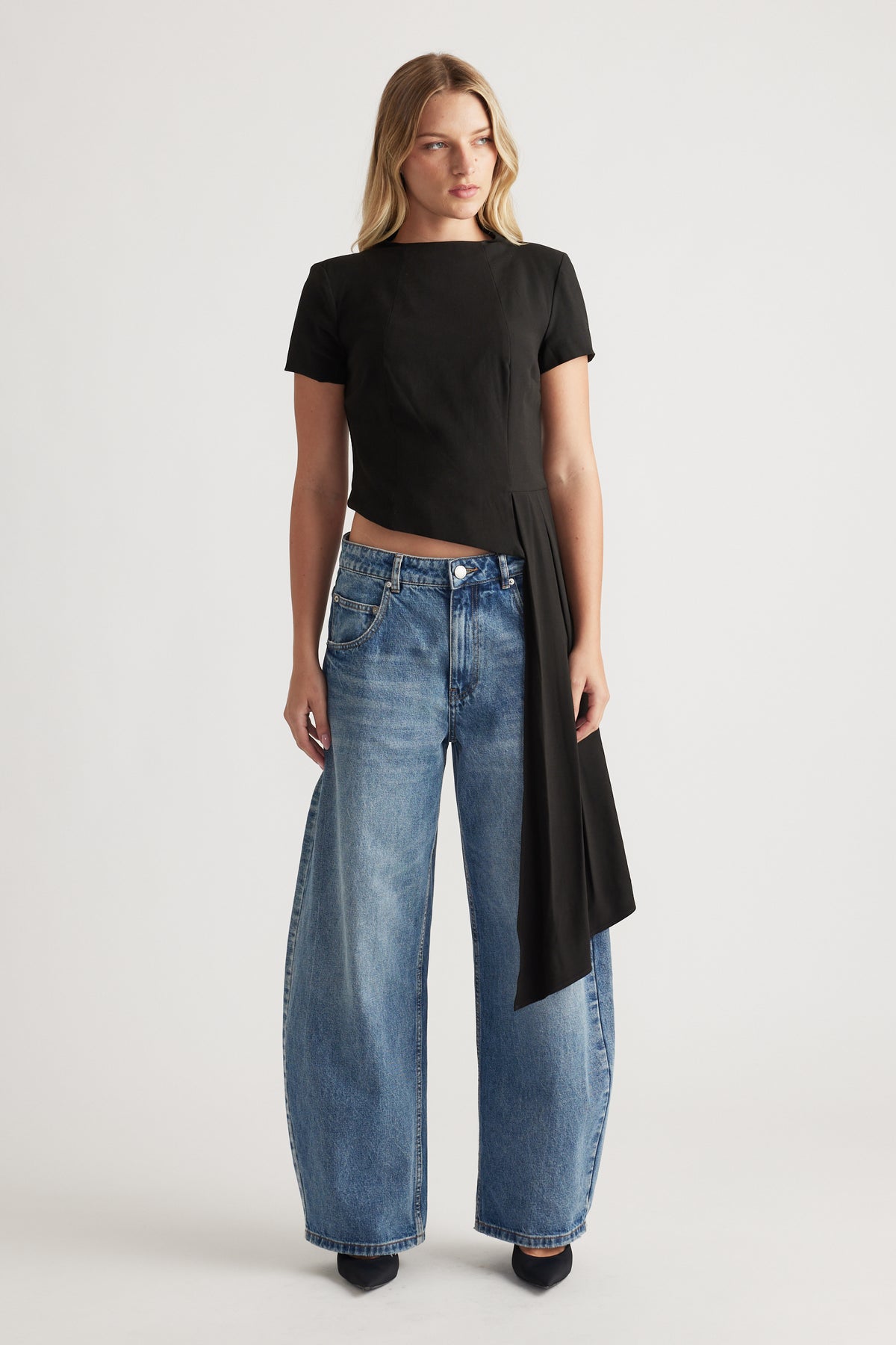 Woman wearing a black short sleeve top with asymmetrical drape detail paired with relaxed wide-leg blue jeans