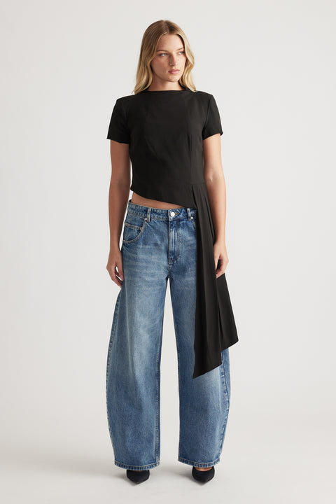 Woman wearing a black short sleeve top with asymmetrical drape detail paired with relaxed wide-leg blue jeans