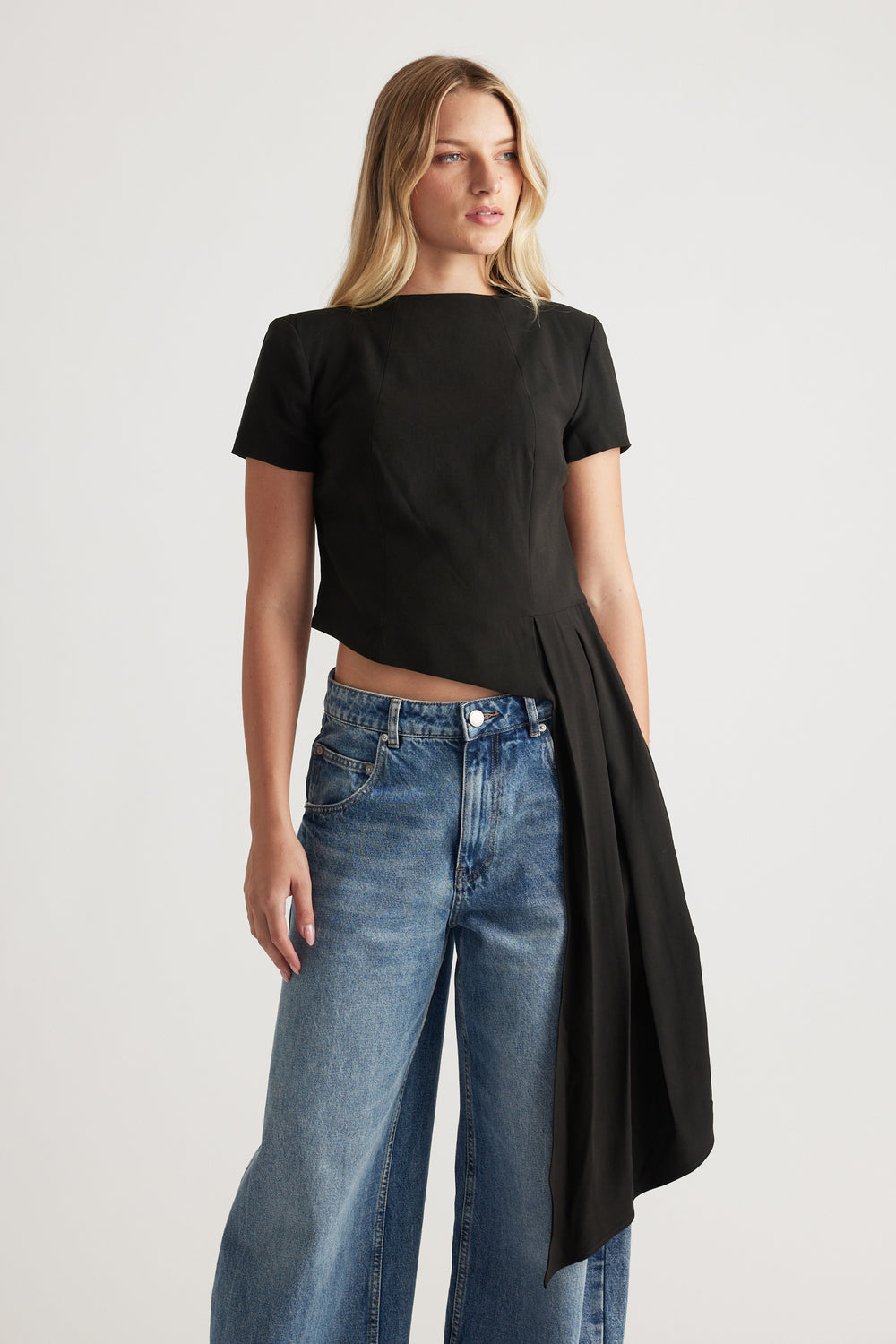 Woman wearing a black short-sleeve top with an asymmetrical draped detail paired with wide-leg blue jeans