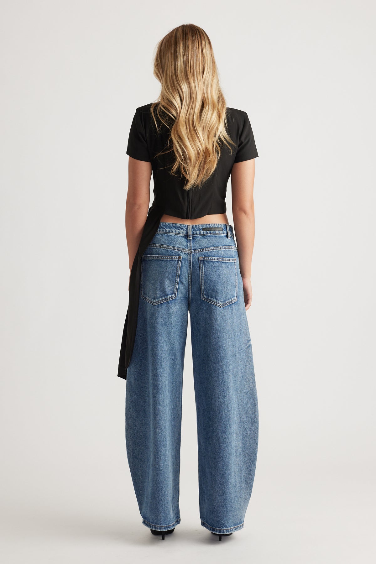 Rear view of a woman wearing relaxed fit mid-blue wide-leg jeans paired with a black short-sleeve draped top