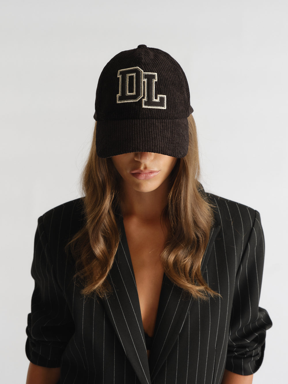 Woman wearing a black D-luxe Kim Cord Cap with "DL" embroidery, paired with a pinstripe blazer for stylish layering.