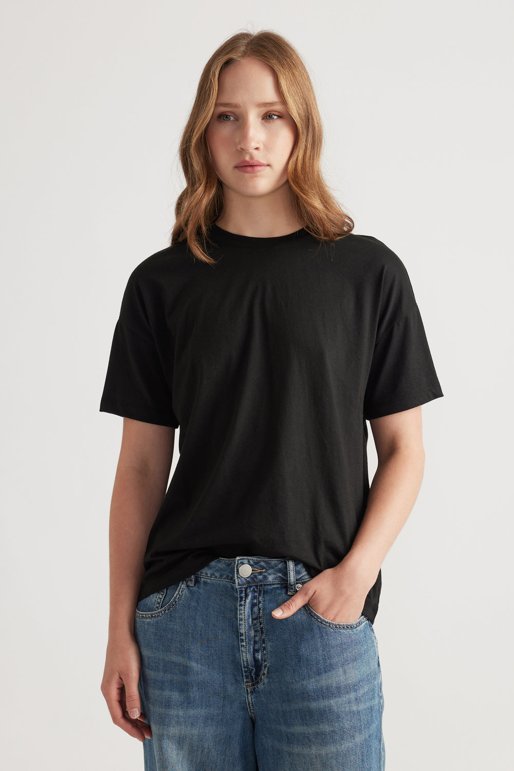 Young woman with loose hair wearing a relaxed black short sleeve tee paired with classic blue denim jeans