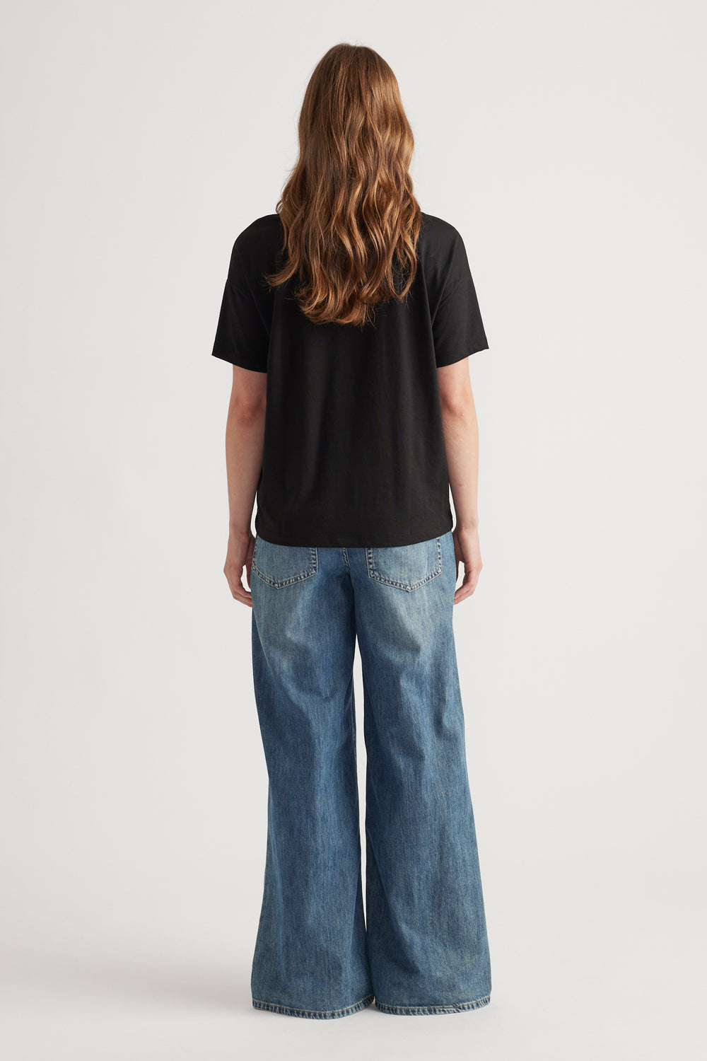 Woman wearing a relaxed black short sleeve tee paired with wide-leg blue denim jeans for a casual look