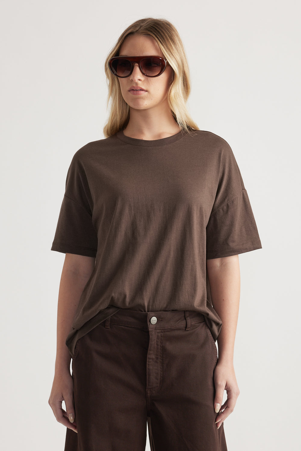 Woman wearing a relaxed brown crew neck short sleeve tee with dark brown jeans and sunglasses