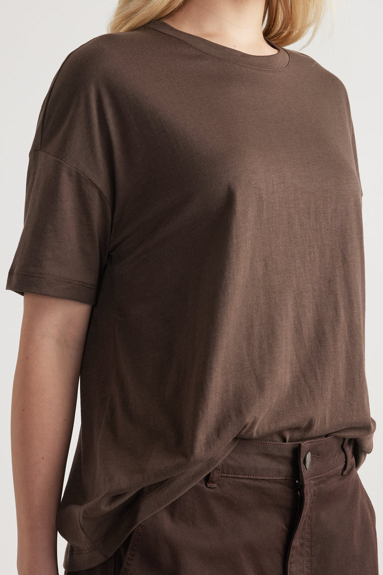 Woman wearing a relaxed dark brown short sleeve crew neck tee with drop shoulders and full length fit