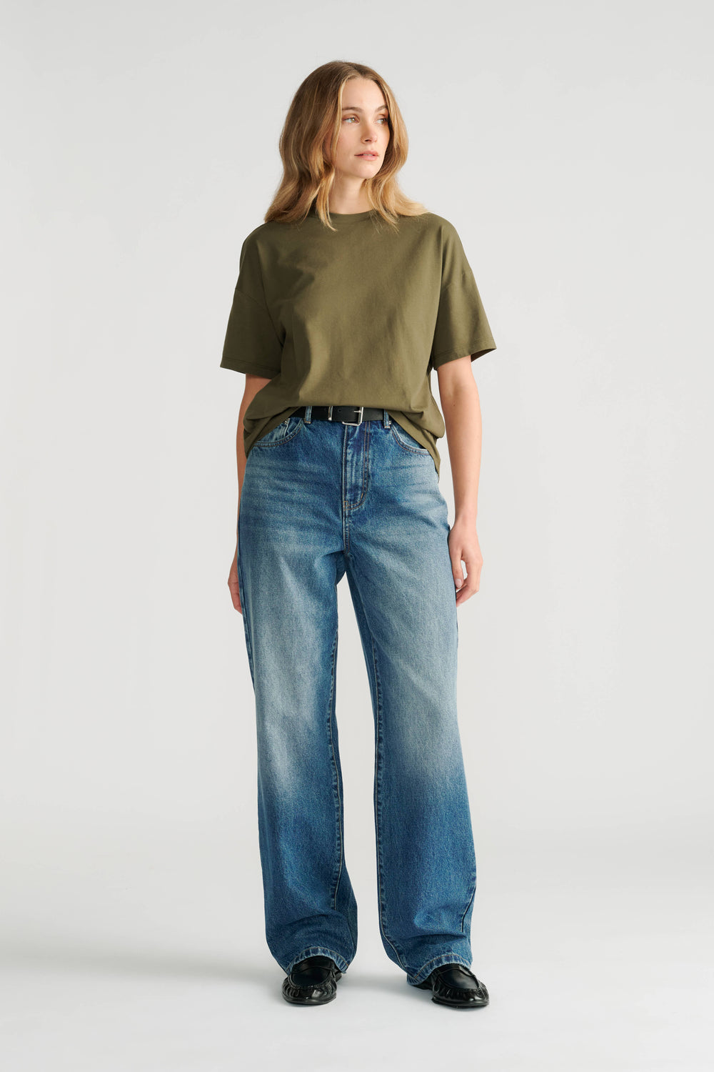 Woman wearing an olive green relaxed short sleeve tee paired with high-rise straight-leg blue jeans and black shoes.