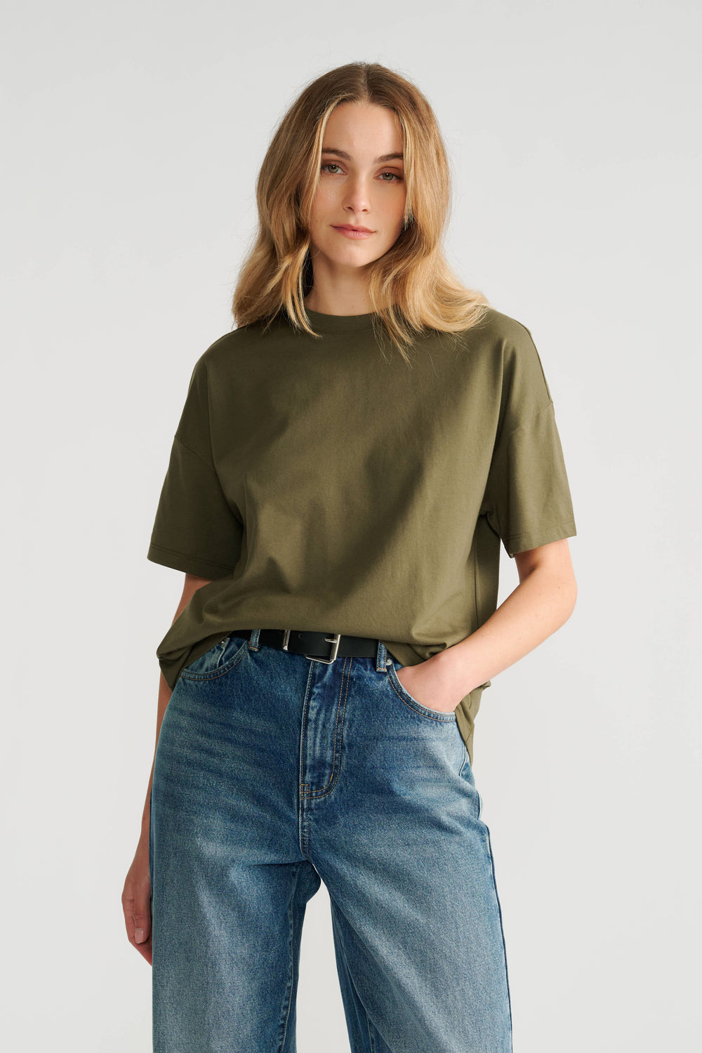 Woman wearing a relaxed fit olive green short sleeve tee paired with high-rise classic blue denim jeans and a black belt