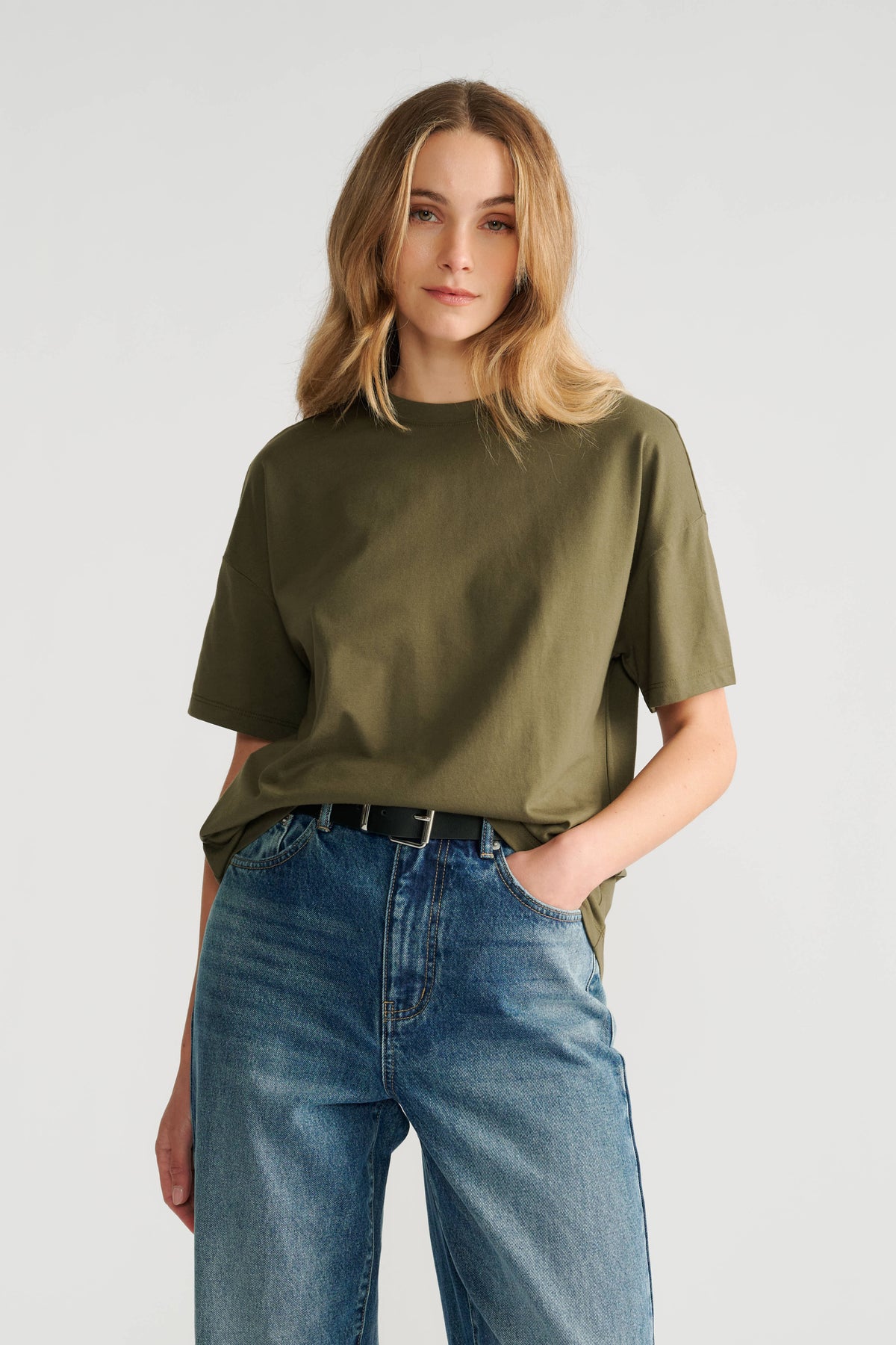 Woman wearing a relaxed fit olive green short sleeve tee paired with high-rise classic blue denim jeans and a black belt