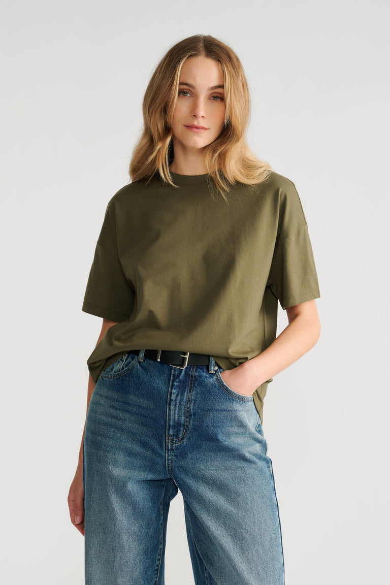 Woman wearing a relaxed fit olive green short sleeve tee paired with high-rise classic blue denim jeans and a black belt