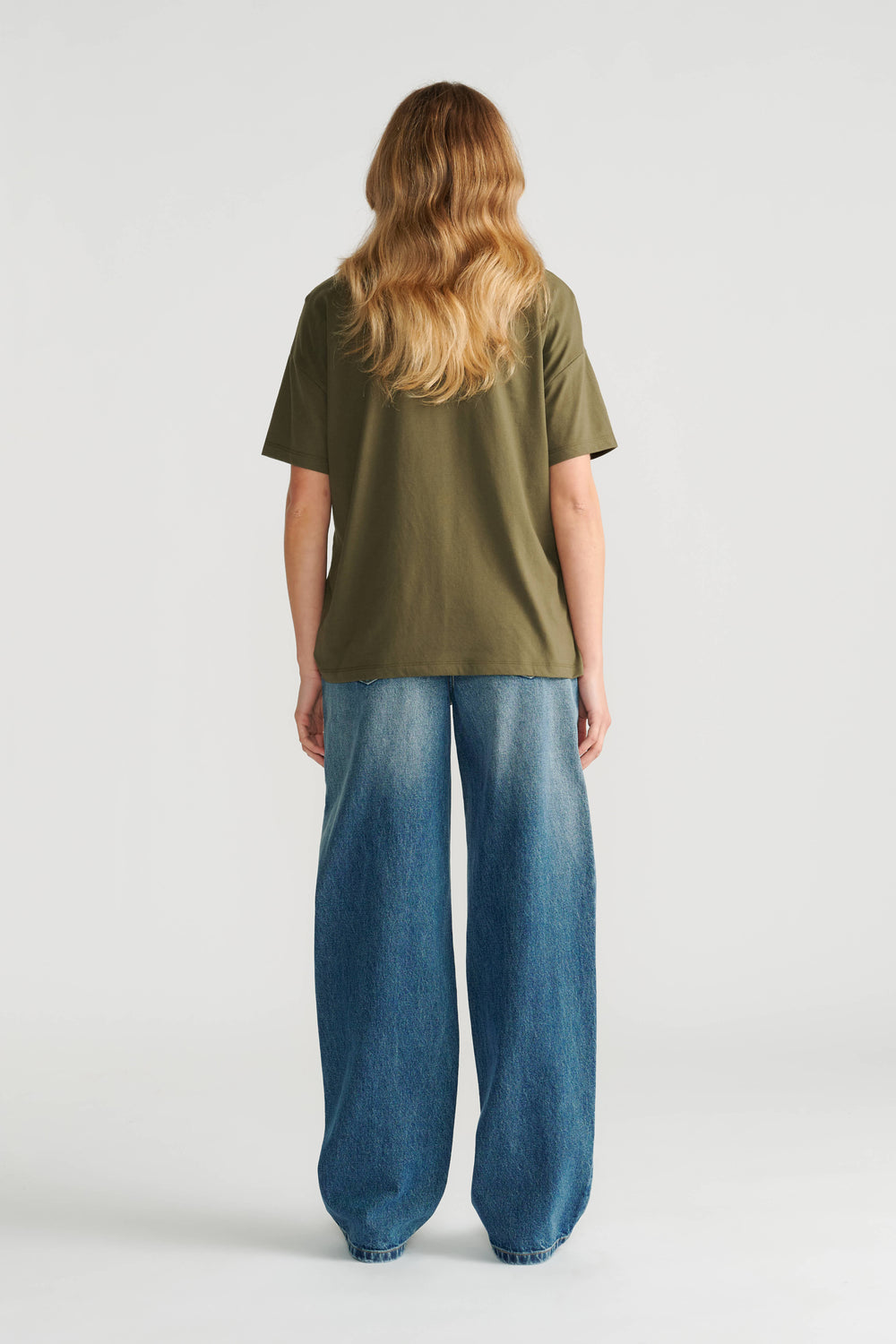 Woman wearing a relaxed olive green short sleeve tee paired with wide-leg blue denim jeans, shown from the back.