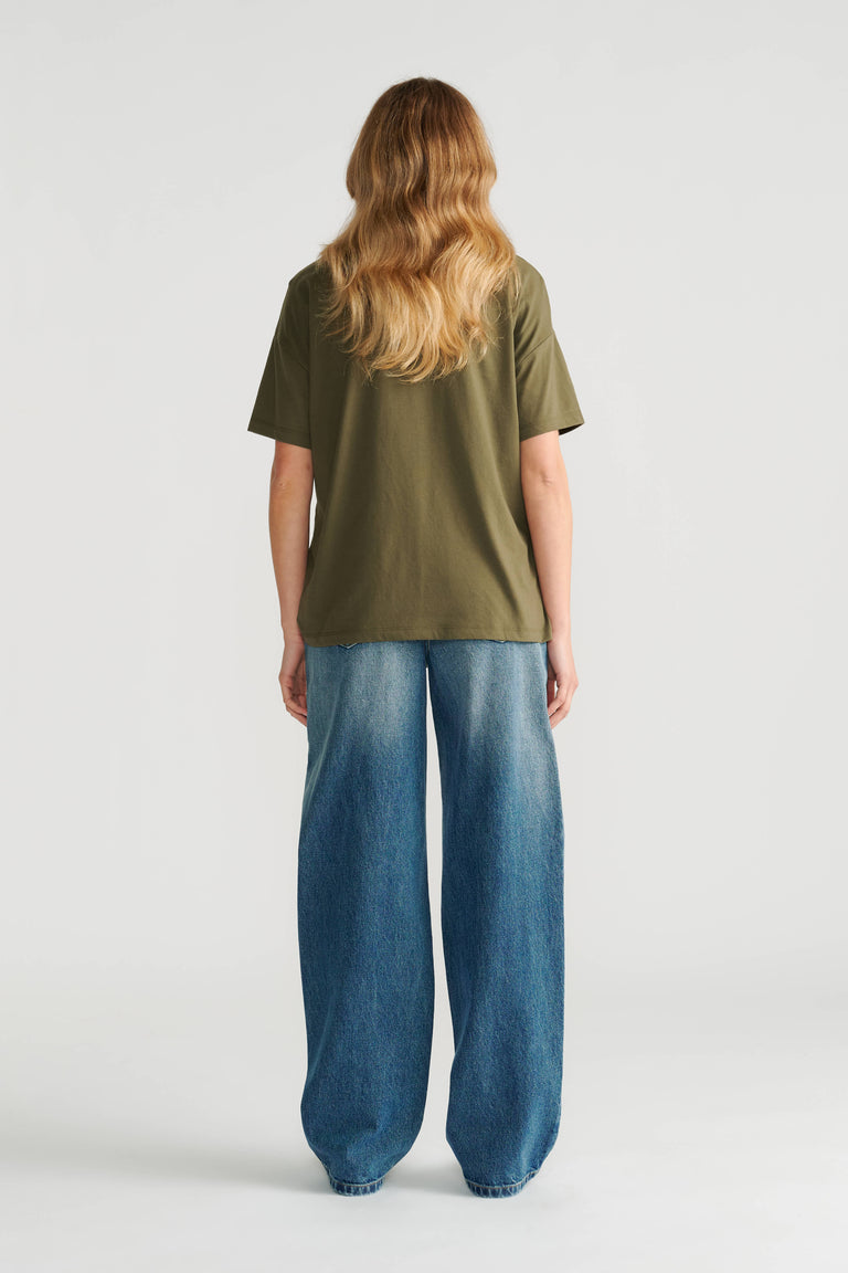 Woman wearing a relaxed olive green short sleeve tee paired with wide-leg blue denim jeans, shown from the back.