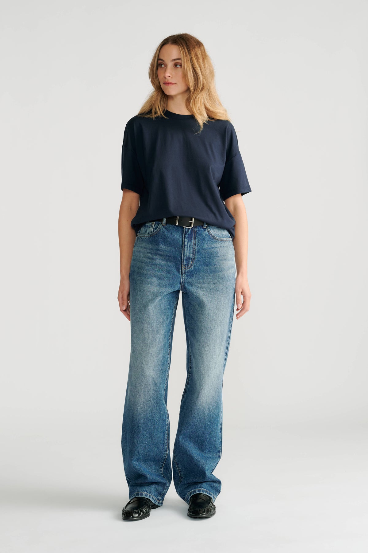 Woman wearing a relaxed navy short sleeve tee paired with high-rise wide-leg faded blue jeans and black shoes.