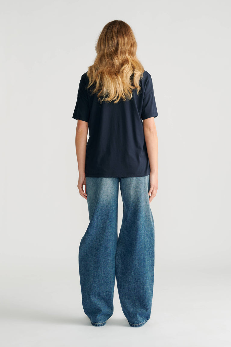 Woman wearing a classic navy short sleeve tee paired with relaxed wide-leg faded blue jeans shown from the back.