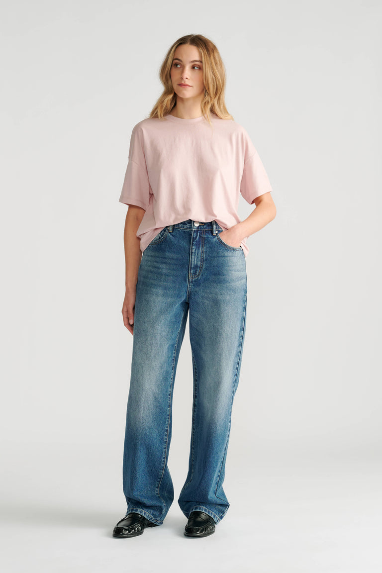 Woman wearing a soft pink relaxed short sleeve tee paired with high-rise straight leg blue jeans and black shoes.