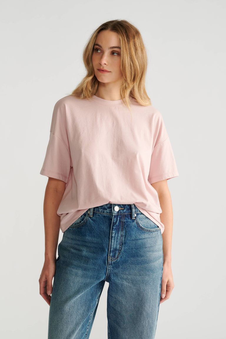 Woman wearing a soft pink relaxed short sleeve tee paired with high-rise classic blue denim jeans.