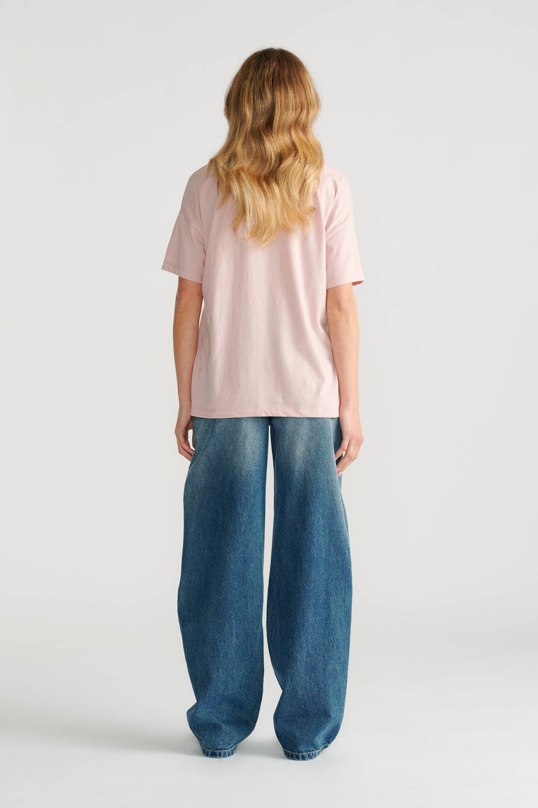Woman wearing a soft pink short sleeve tee paired with loose, wide-leg blue denim jeans shown from behind