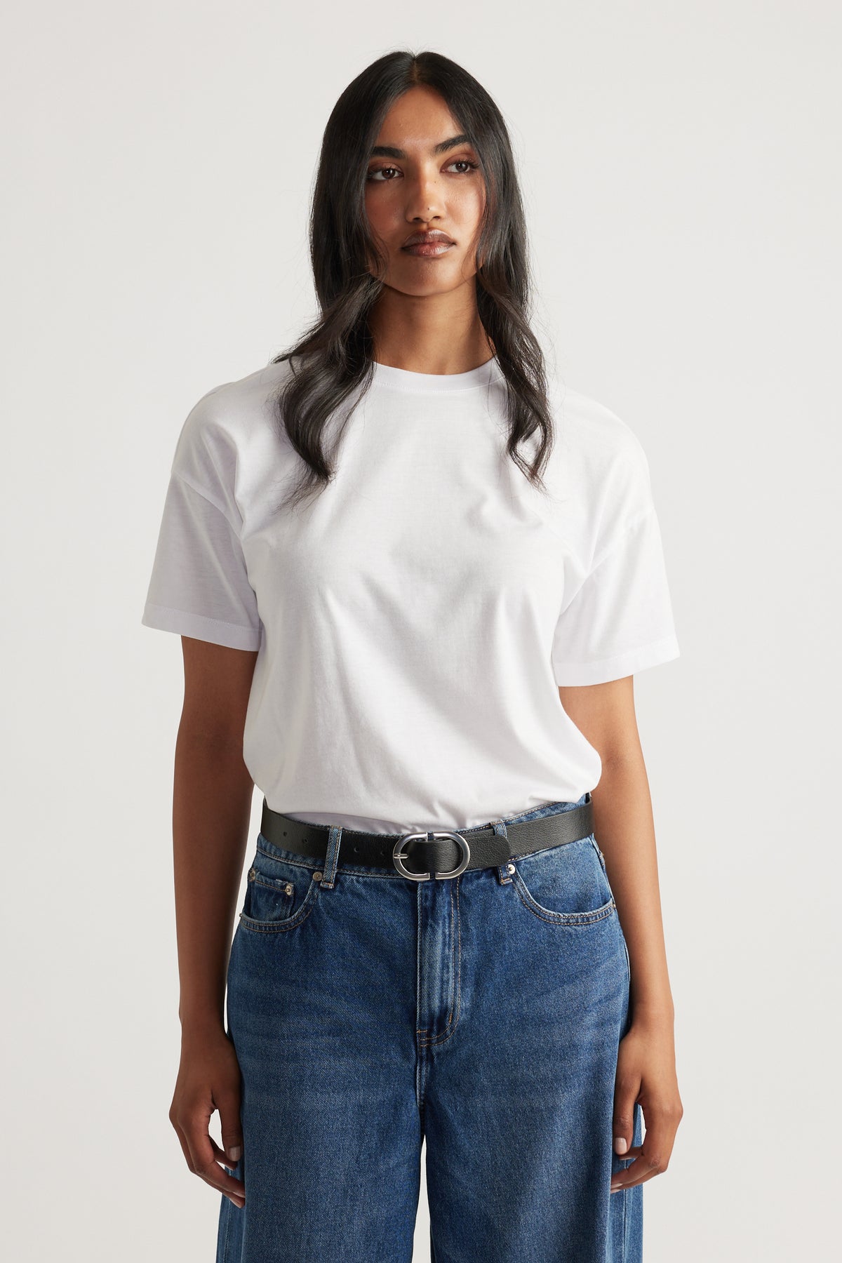 Woman wearing a relaxed white short sleeve tee tucked into high-waisted blue denim jeans with a black belt