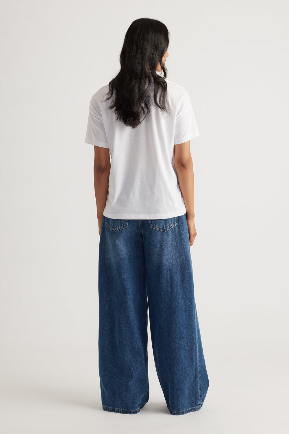 Person wearing a relaxed white short sleeve tee paired with wide-leg blue denim pants for a casual look