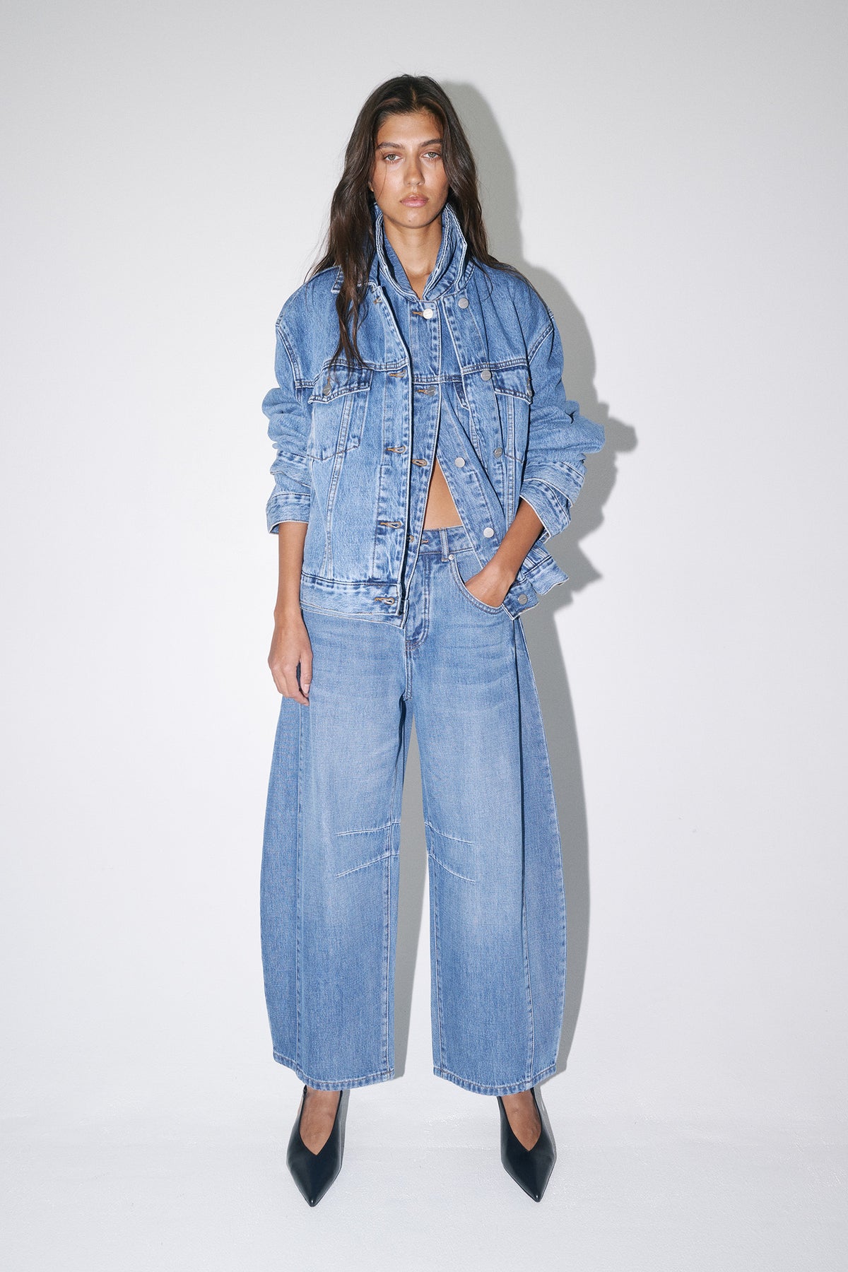 Woman wearing a light wash denim jacket with cropped barrel jeans and black pointed-toe heels