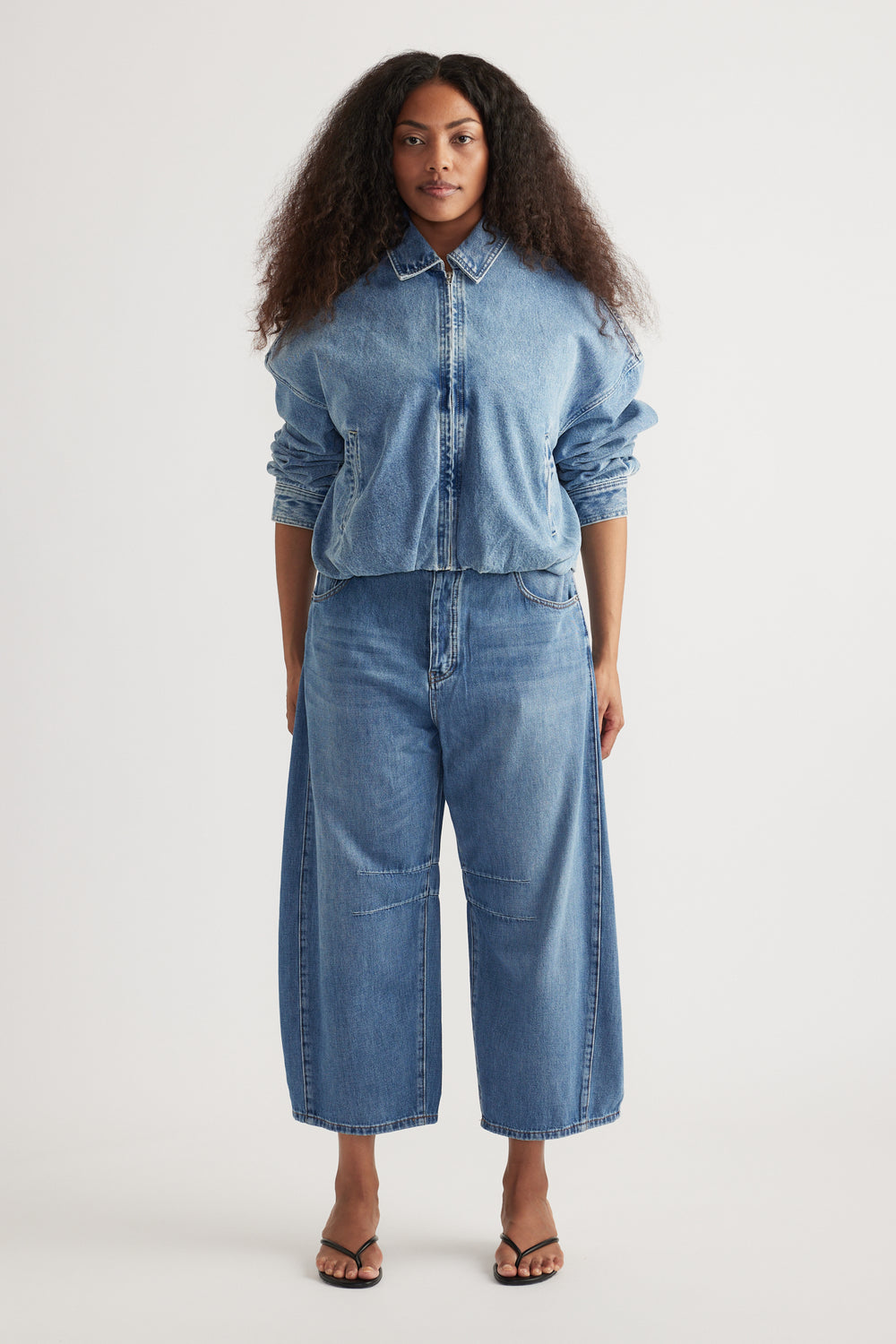 Woman wearing a blue denim zip-front shirt with cropped barrel-leg jeans and black sandals