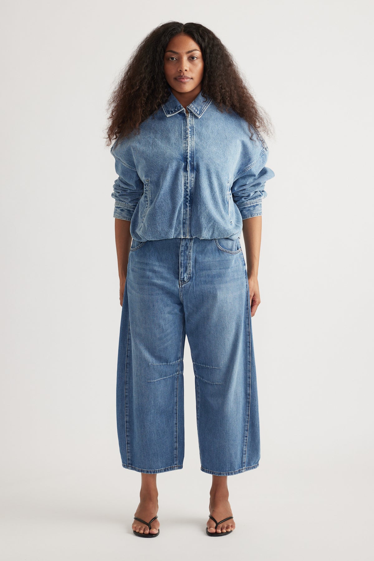 Woman wearing a blue denim zip-front shirt with cropped barrel-leg jeans and black sandals