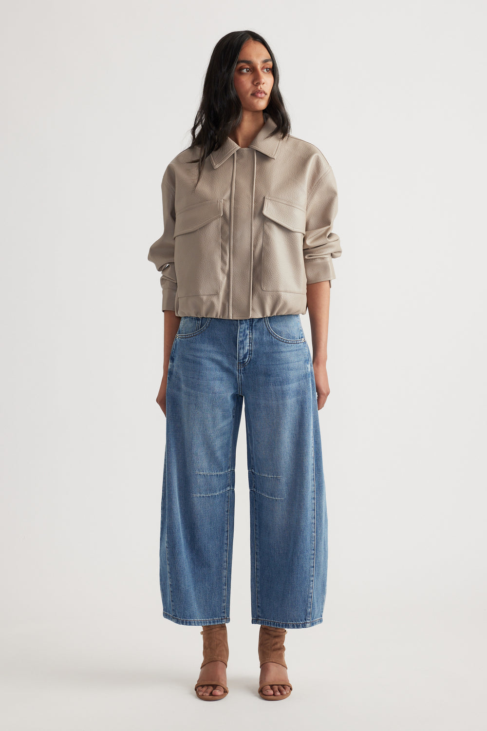 Woman wearing a beige cropped jacket with large pockets paired with relaxed wide-leg blue jeans and open-toe heels