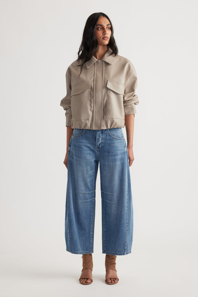 Woman wearing a beige cropped jacket with large pockets paired with relaxed wide-leg blue jeans and open-toe heels