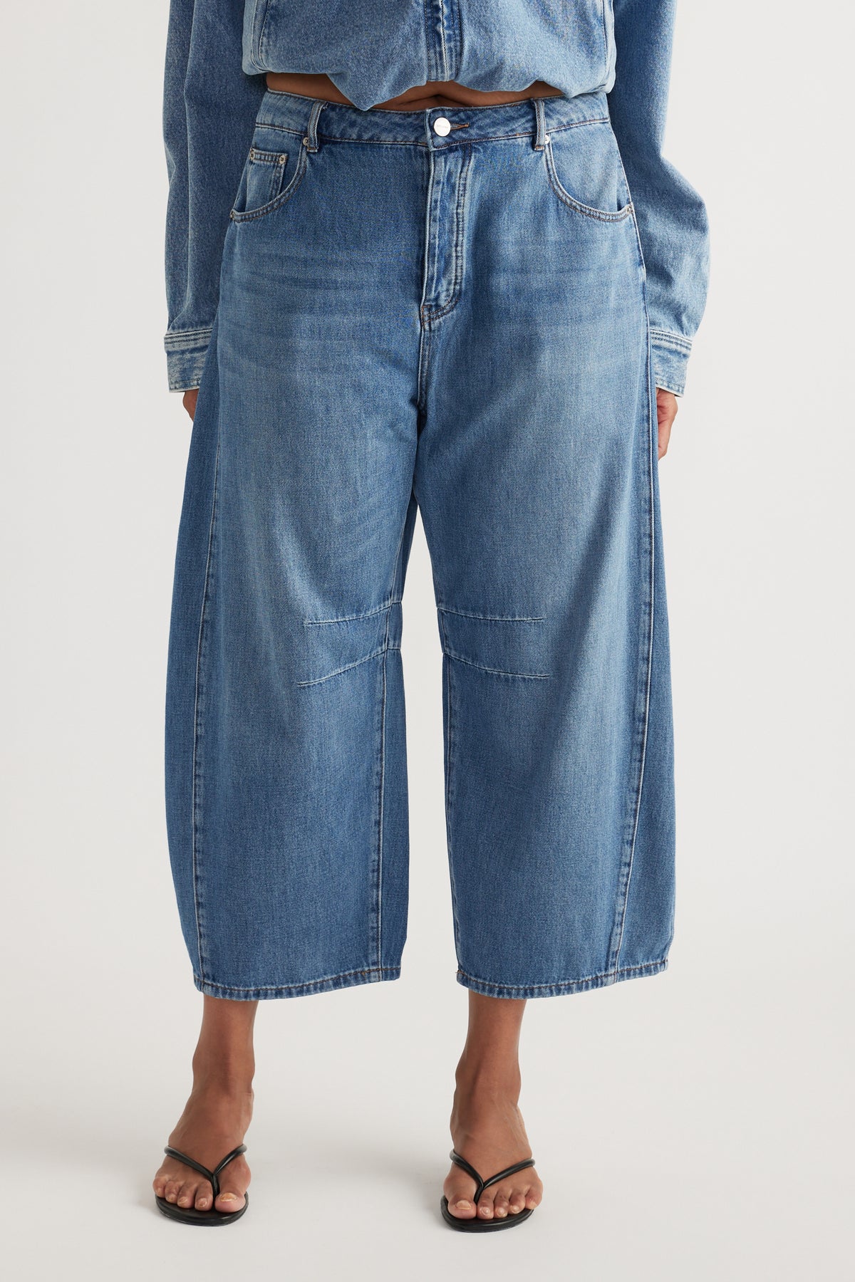Woman wearing high-rise cropped blue barrel-leg jeans with a relaxed fit and black thong sandals