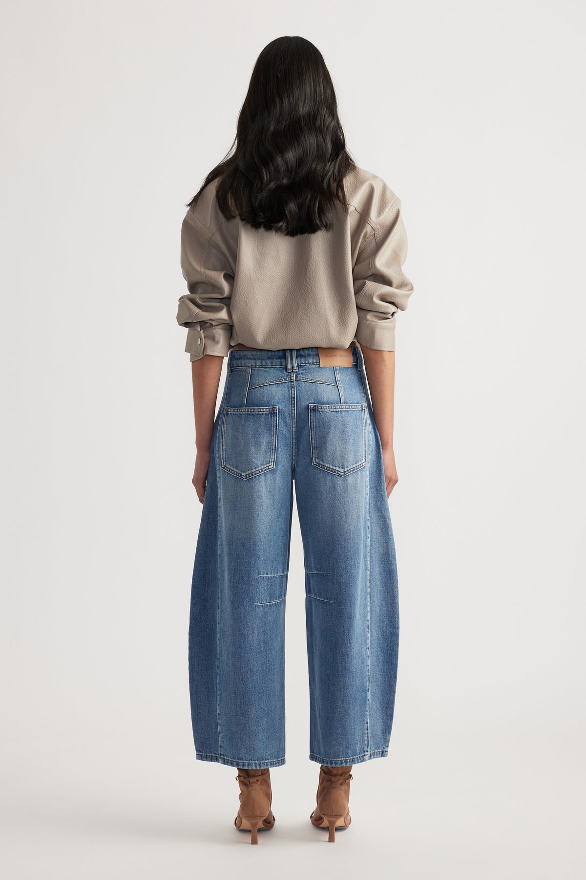 Back view of woman wearing relaxed fit blue jeans paired with a taupe oversized sweatshirt and heeled boots