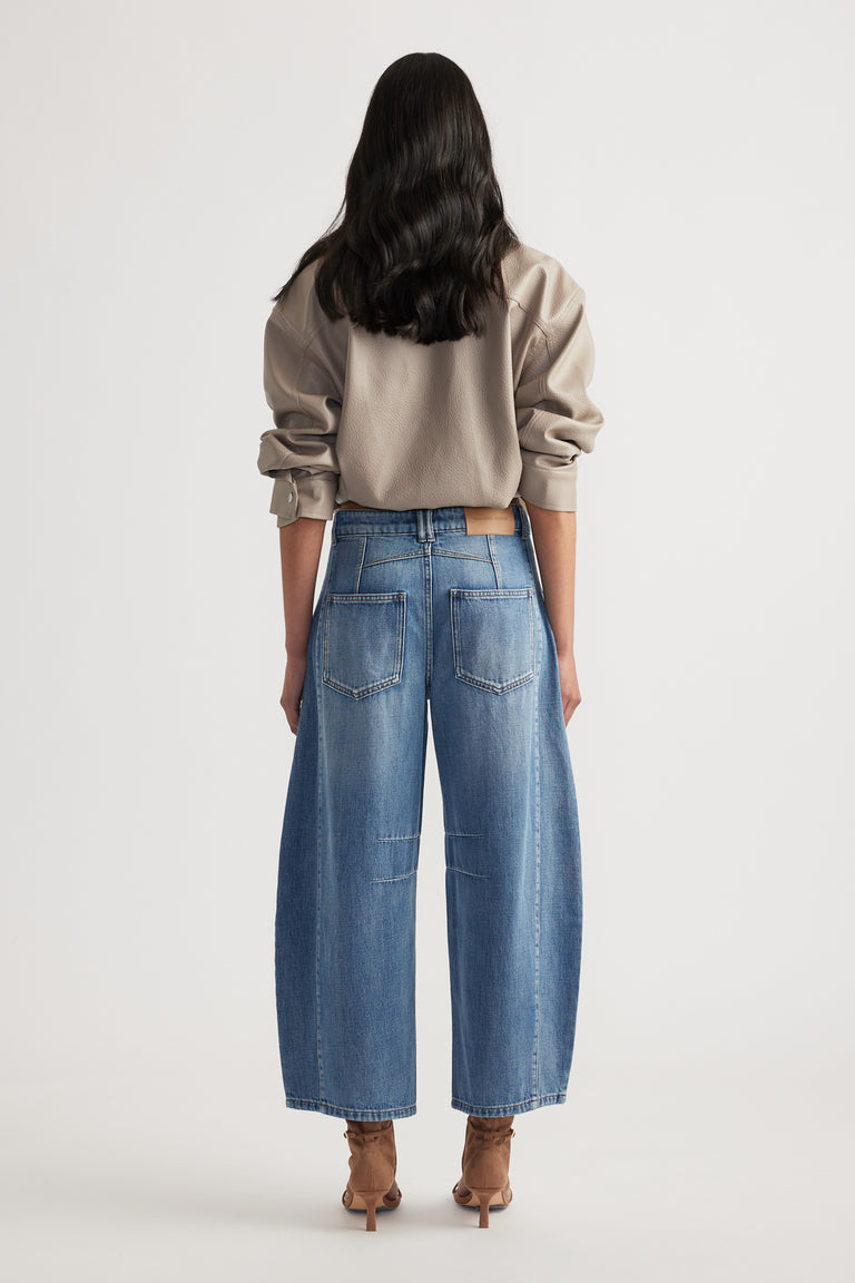 Back view of woman wearing relaxed fit blue jeans paired with a taupe oversized sweatshirt and heeled boots