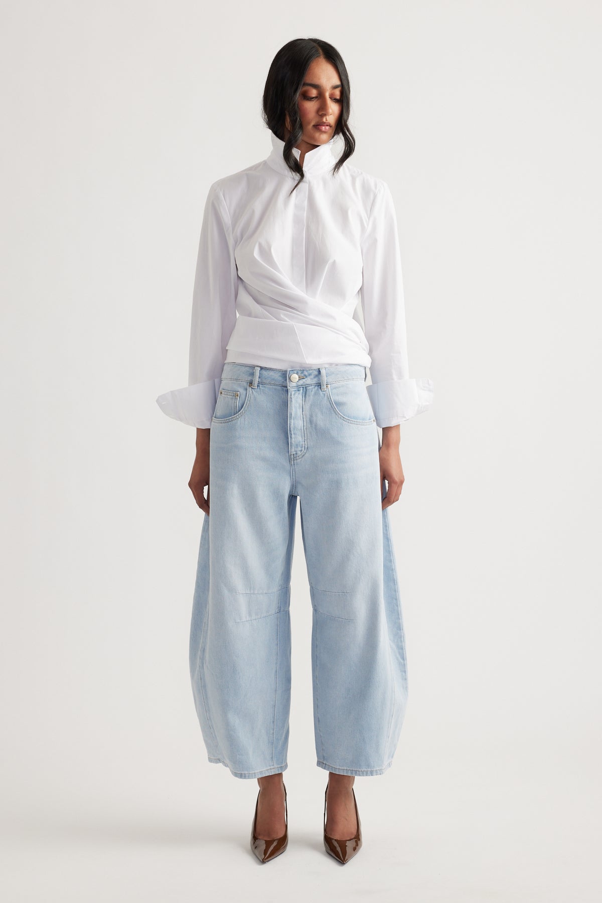 Woman wearing light wash wide-leg jeans paired with a white high-neck blouse, styled with pointed brown heels.