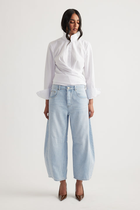 Woman wearing light wash wide-leg jeans paired with a white high-neck blouse, styled with pointed brown heels.