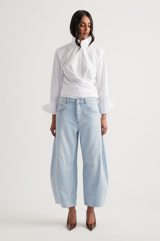 Woman wearing light wash wide-leg jeans paired with a white high-neck blouse, styled with pointed brown heels.