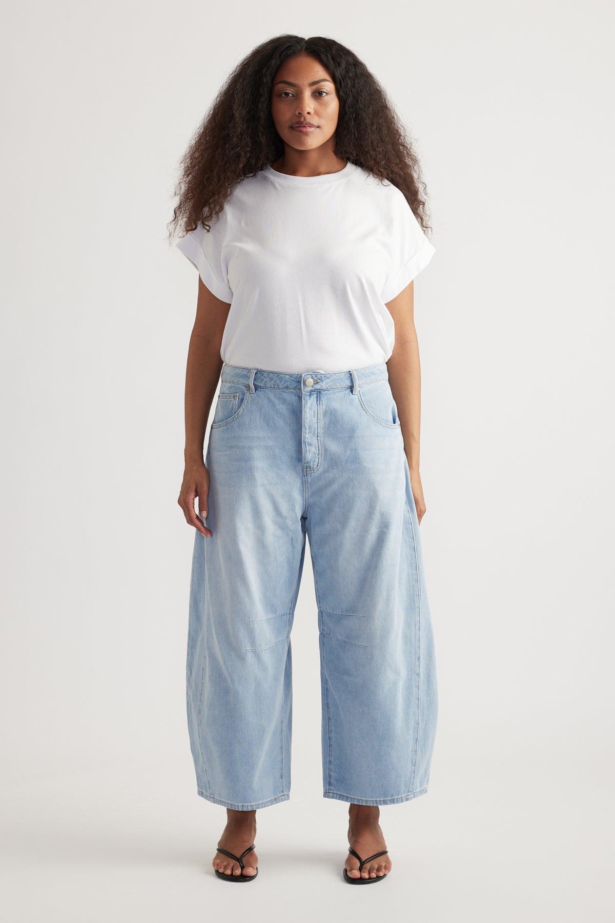 Woman wearing a white tee with high rise cropped light blue barrel leg jeans and flat sandals
