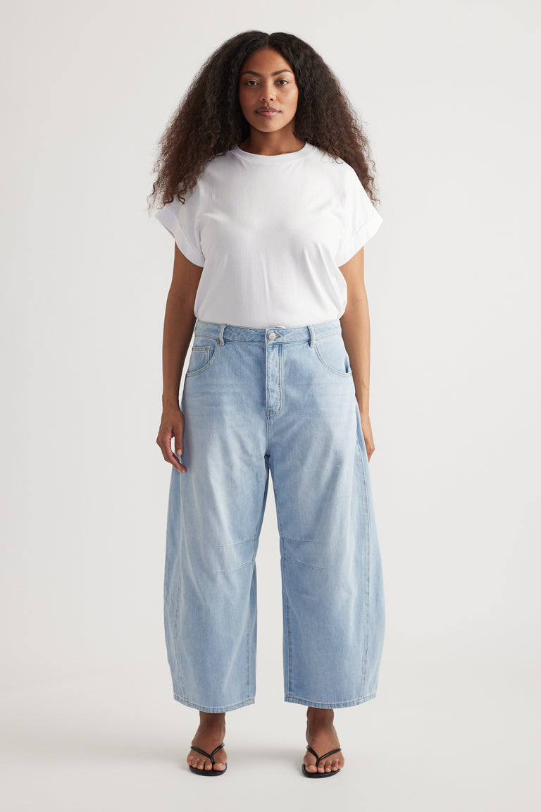 Woman wearing a white tee with high rise cropped light blue barrel leg jeans and flat sandals