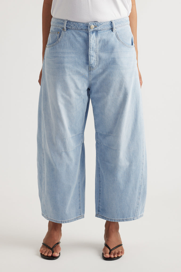 Woman wearing light blue high rise cropped barrel jeans with a white top and black strappy sandals
