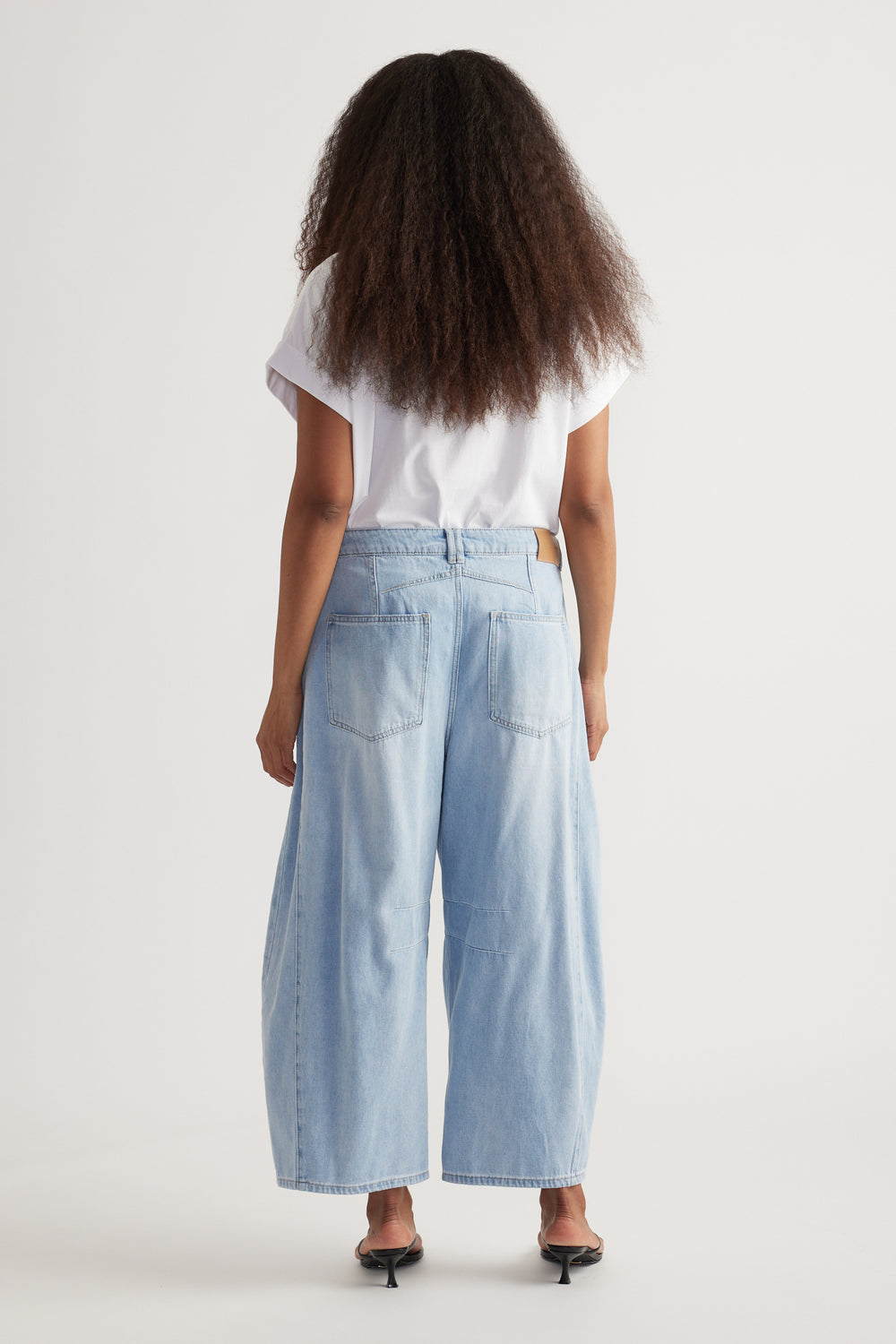 Back view of woman wearing high rise cropped light blue barrel-leg jeans with a white tee and kitten heels