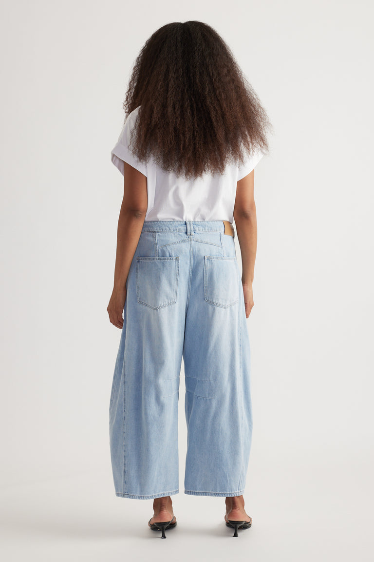 Back view of woman wearing high rise cropped light blue barrel-leg jeans with a white tee and kitten heels