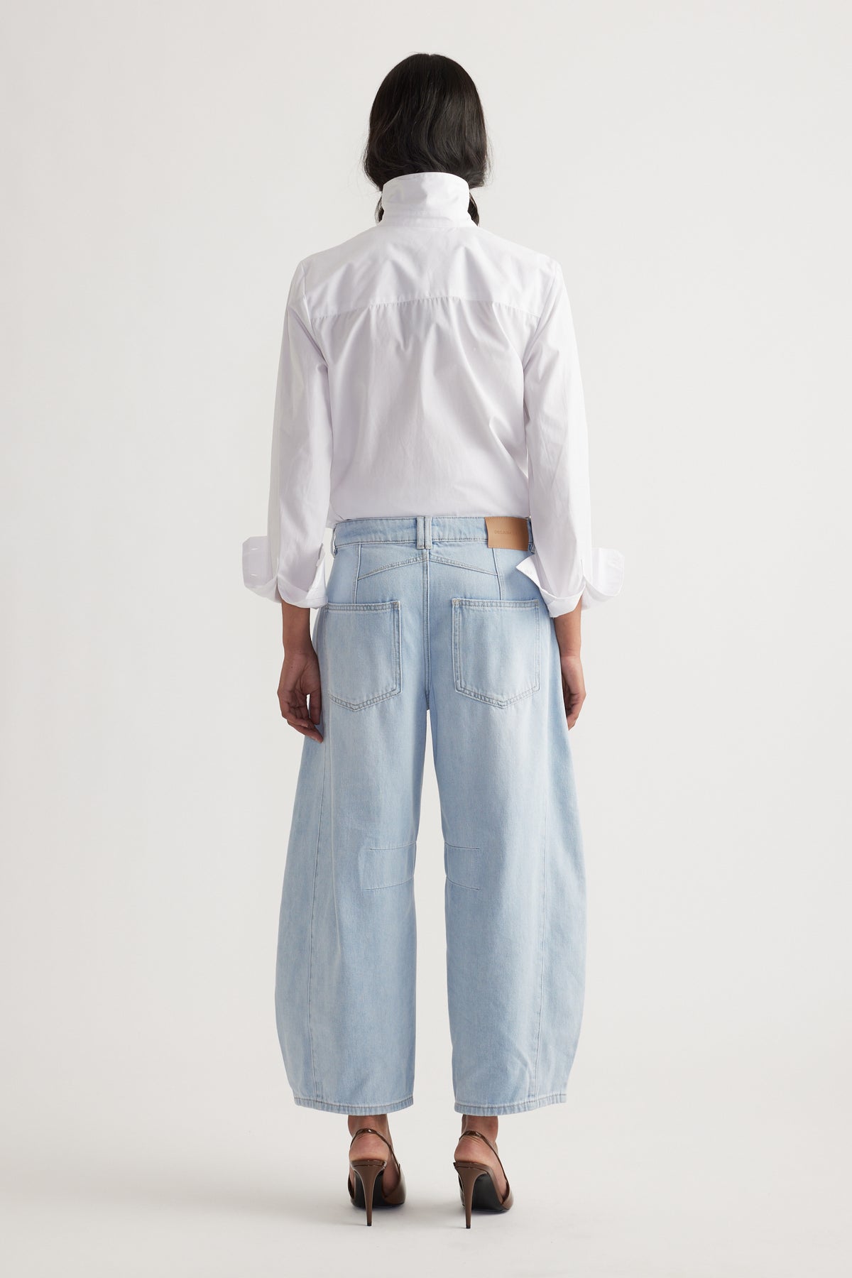Back view of relaxed light wash wide-leg jeans paired with a crisp white shirt and heels in soft lighting