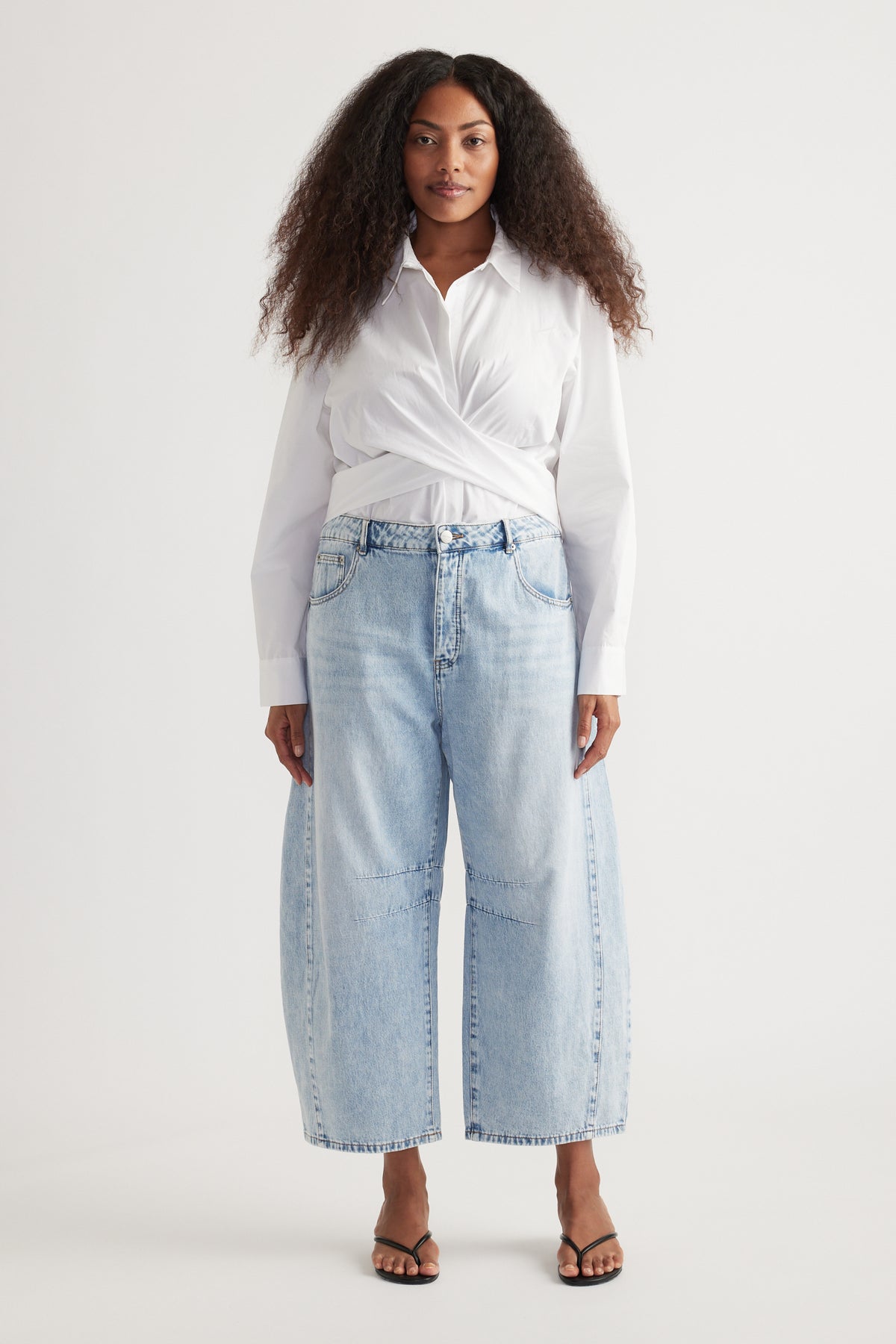 Woman wearing a white twist-front blouse with light wash cropped barrel jeans and strappy sandals