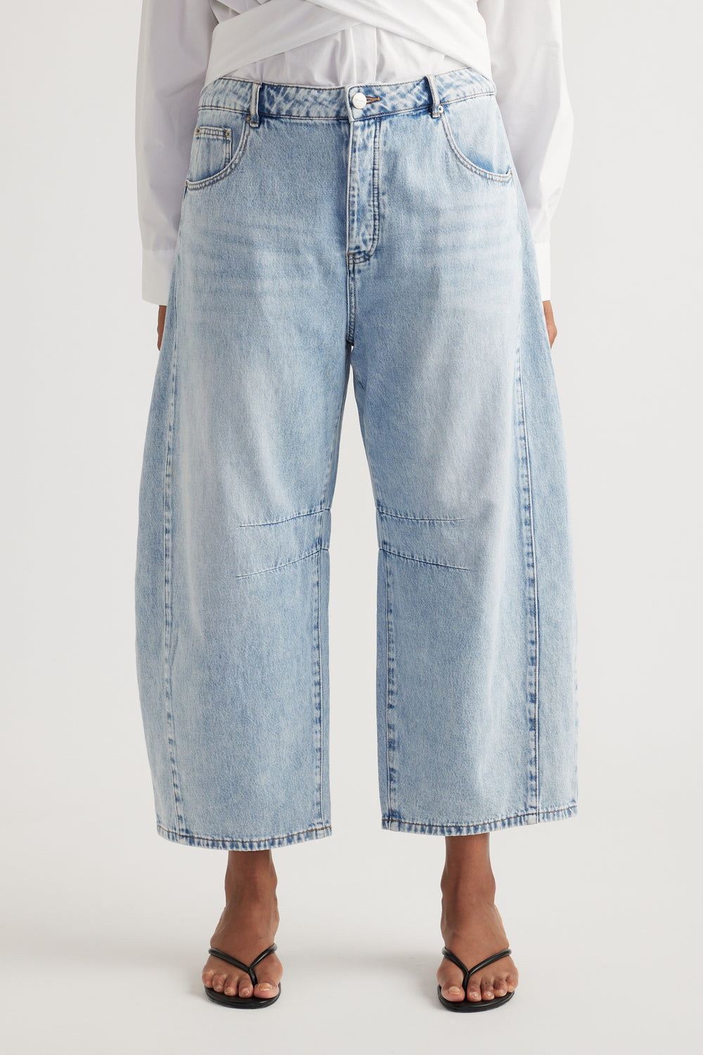 Woman wearing high rise light blue cropped barrel jeans with a white shirt and black sandals
