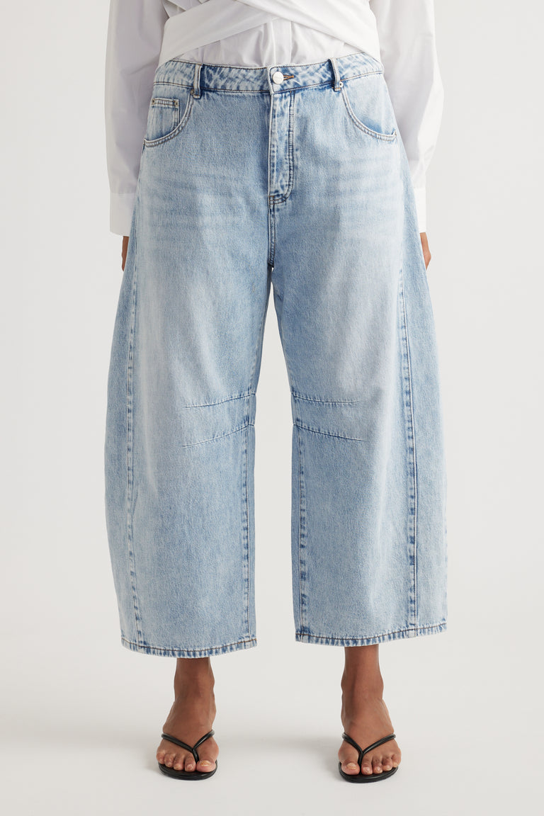 Woman wearing high rise light blue cropped barrel jeans with a white shirt and black sandals