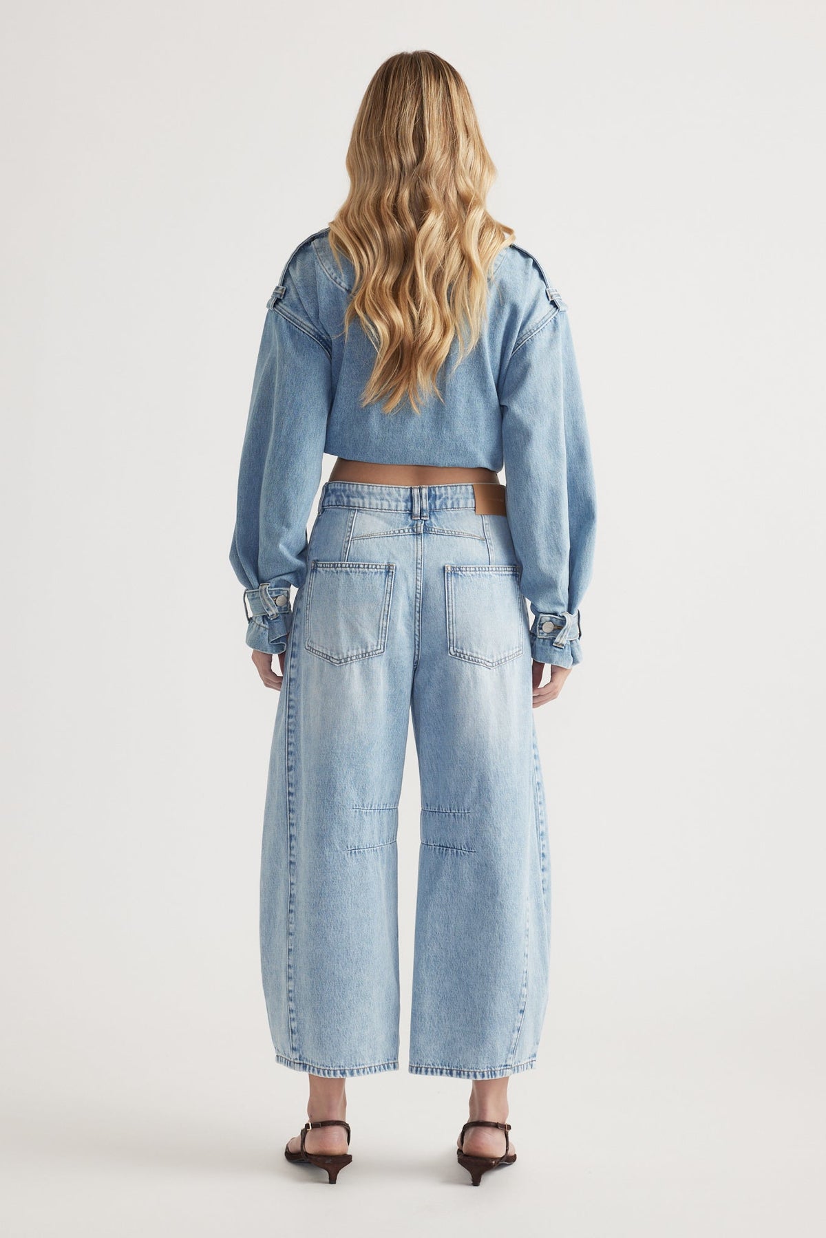 Woman wearing light wash high-rise wide-leg jeans paired with a matching cropped denim jacket and heels