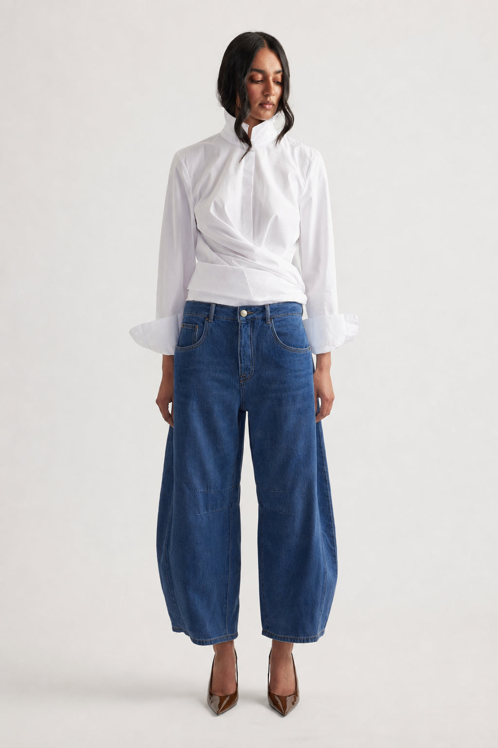 Woman wearing dark blue wide-leg jeans paired with a white long-sleeve blouse and brown pointed heels, front view
