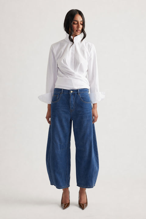 Woman wearing dark blue wide-leg jeans paired with a white long-sleeve blouse and brown pointed heels, front view